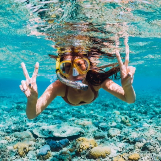Snorkeler shows peace signs with hands underwater.